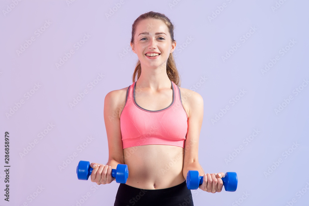 Young woman with two dumbbells in hands, standing on a purple background. Fitness exercise. Young woman with two dumbbells in hands, standing on a purple background. Fitness exercise.