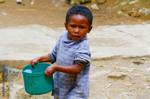 Poor malagasy boy carrying plastic bucket - poverty photo