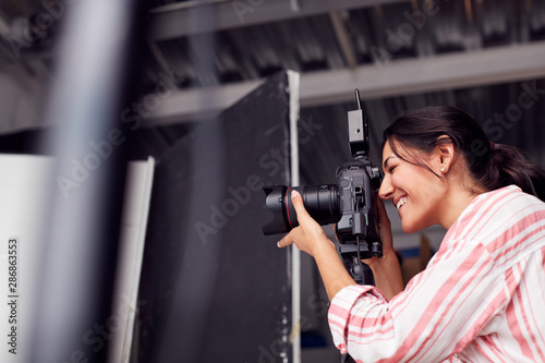 Female Photographer With Camera On Photo Shoot Against White Studio Backdrop