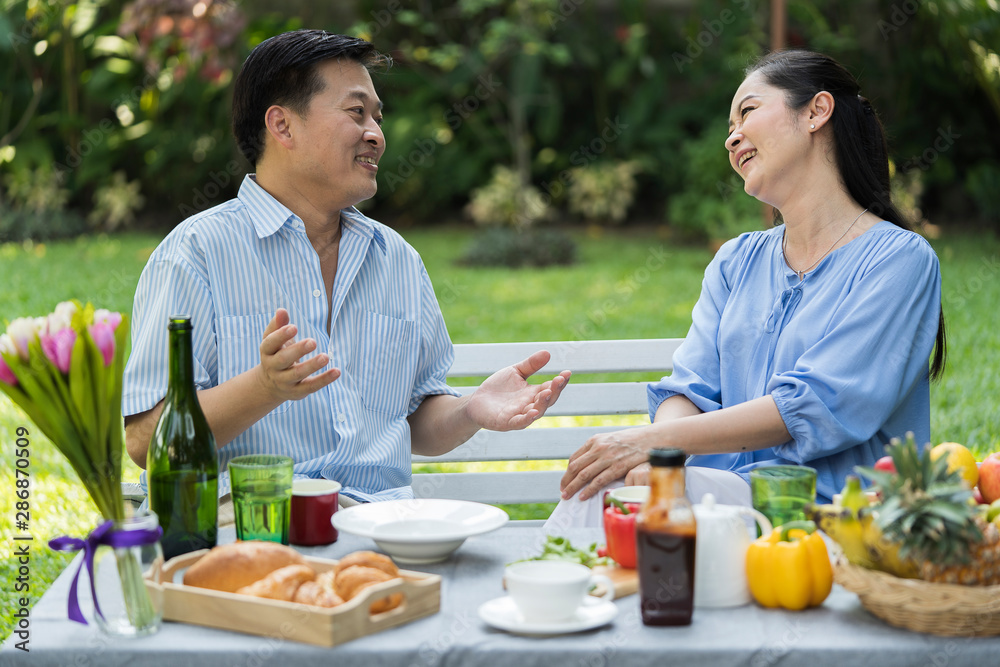 Lovely springtime picnic senior Asian couple enjoying eating morning Breakfast Togetherness in the city park outdoors. Beautiful nature. Retirement, happy or Aged Society concept