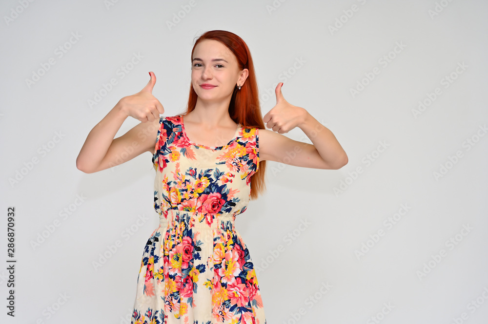 Portrait of a pretty red-haired girl, a happy young woman in a bright summer dress on a white background in the studio. Smiling, showing different emotions. Portrait of a pretty red-haired girl, a happy young woman in a bright summer dress on a white background in the studio. Smiling, showing different emotions.