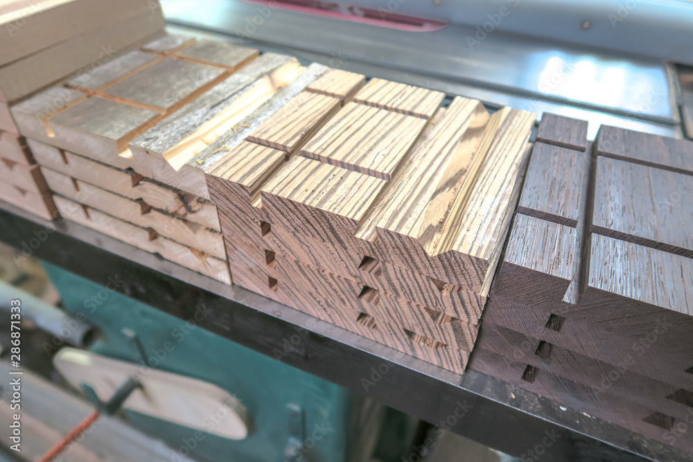 Obraz premium Closeup of stacked and sorted production pieces of exotic wood with various machined cuts and grooves for a woodworking project sitting on a table saw.