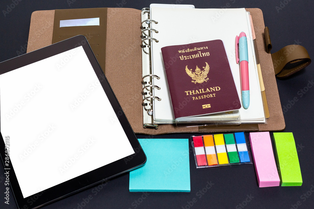Passport and tablet on planner with pen and note pad