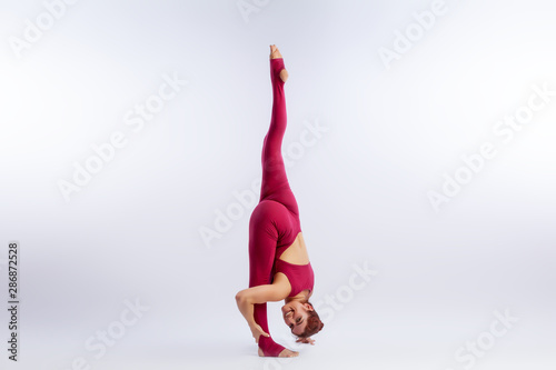 Beautiful slim woman in sports overalls doing yoga, standing in an asana balancing pose on white isolated background. The concept of sports and meditation.