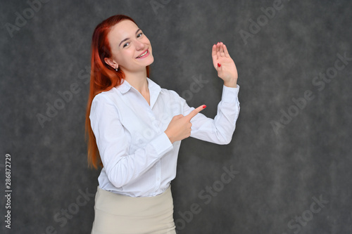 Portrait of a pretty red-haired girl, a happy young woman manager in a light business suit on a gray background in the studio. Smiling, showing different emotions.