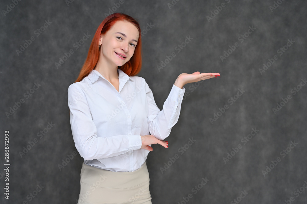 Portrait of a pretty red-haired girl, a happy young woman manager in a light business suit on a gray background in the studio. Smiling, showing different emotions. Portrait of a pretty red-haired girl, a happy young woman manager in a light business suit on a gray background in the studio. Smiling, showing different emotions.