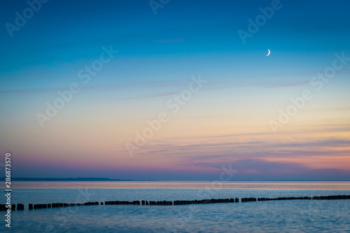 Mondsichel über Ostsee mit Buhne am Abend photo