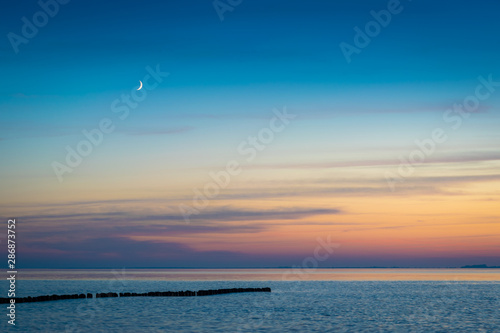 Mondsichel   ber Ostsee mit Buhne am Abend