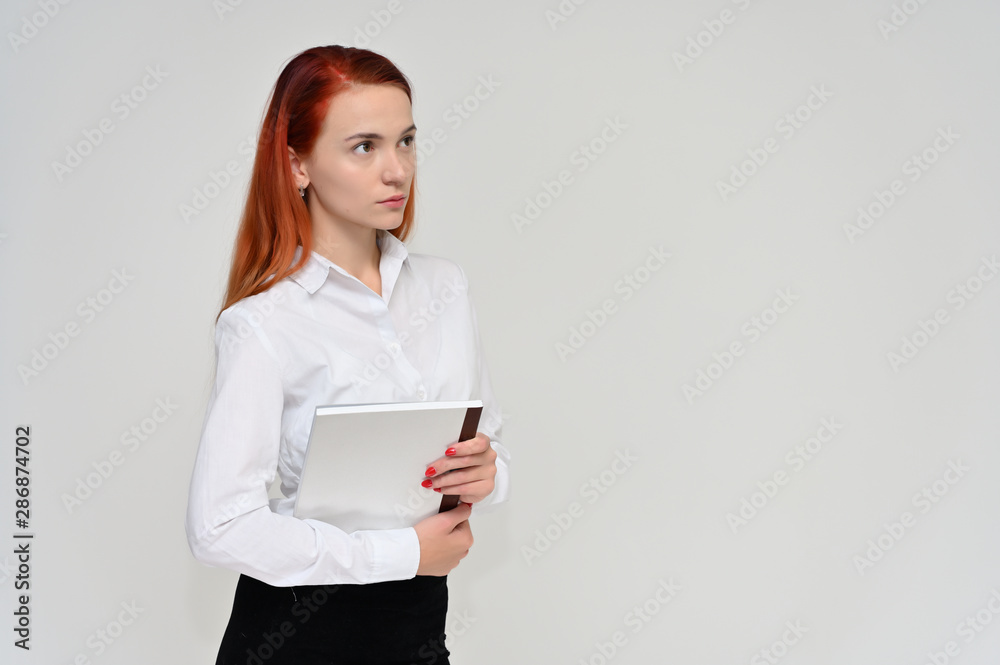 Portrait of a pretty red-haired girl, a happy young woman manager in a business suit on a white background in studio. Smiling, showing different emotions. Portrait of a pretty red-haired girl, a happy young woman manager in a business suit on a white background in studio. Smiling, showing different emotions.