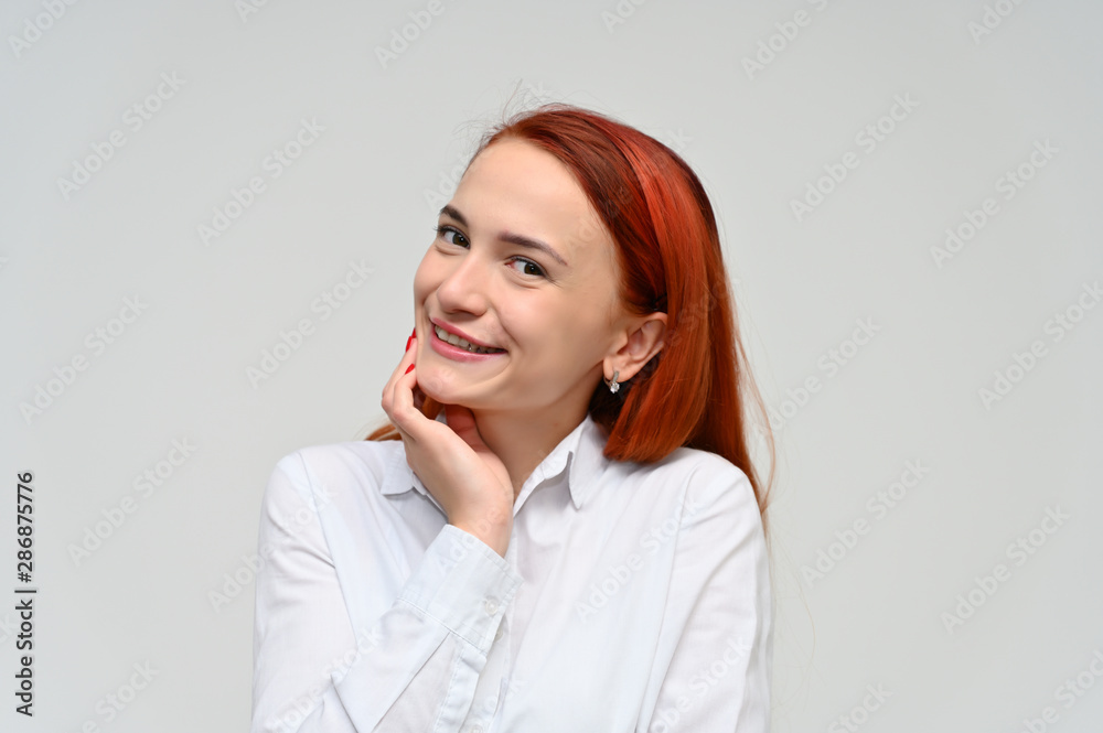 Close-up Portrait of a pretty red-haired girl, a happy young woman manager in a white shirt on a white background in studio. Smiling, showing different emotions. Close-up Portrait of a pretty red-haired girl, a happy young woman manager in a white shirt on a white background in studio. Smiling, showing different emotions.
