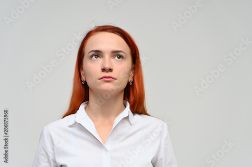 Close-up Portrait of a pretty red-haired girl  a happy young woman manager in a white shirt on a white background in studio. Smiling  showing different emotions.