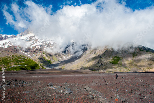 A young woman with backpack hiking on iceberg and snow and enjoying the views of the Antuco volcano black volcano desert. Northern Patagonia, Andes, Chile, South America. photo