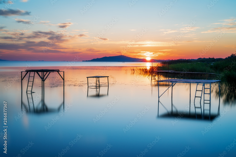 sunrise with sun peaking out of the mountain at lake balaton hungery, with nice reflections in the water fonyód district hungary summer vacation travel relax