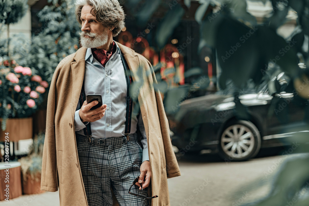 Obraz premium Elegant senior man with smartphone standing on the street