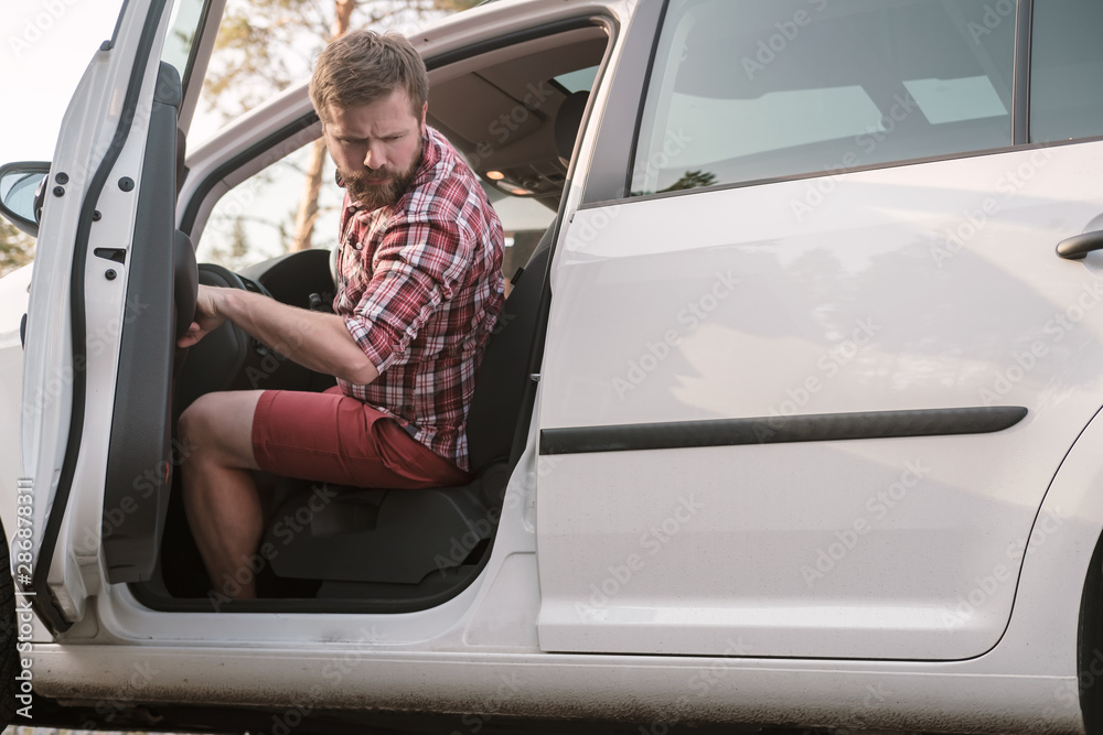 A male driver sits behind the wheel of a car with an open door and looks back at problems with the wheel of the car. A male driver sits behind the wheel of a car with an open door and looks back at problems with the wheel of the car.