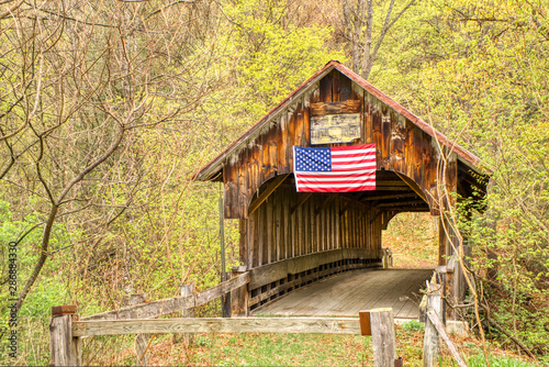A covered bridge, long abandoned, still stands in the countryside despite being neglected with weathered wood.