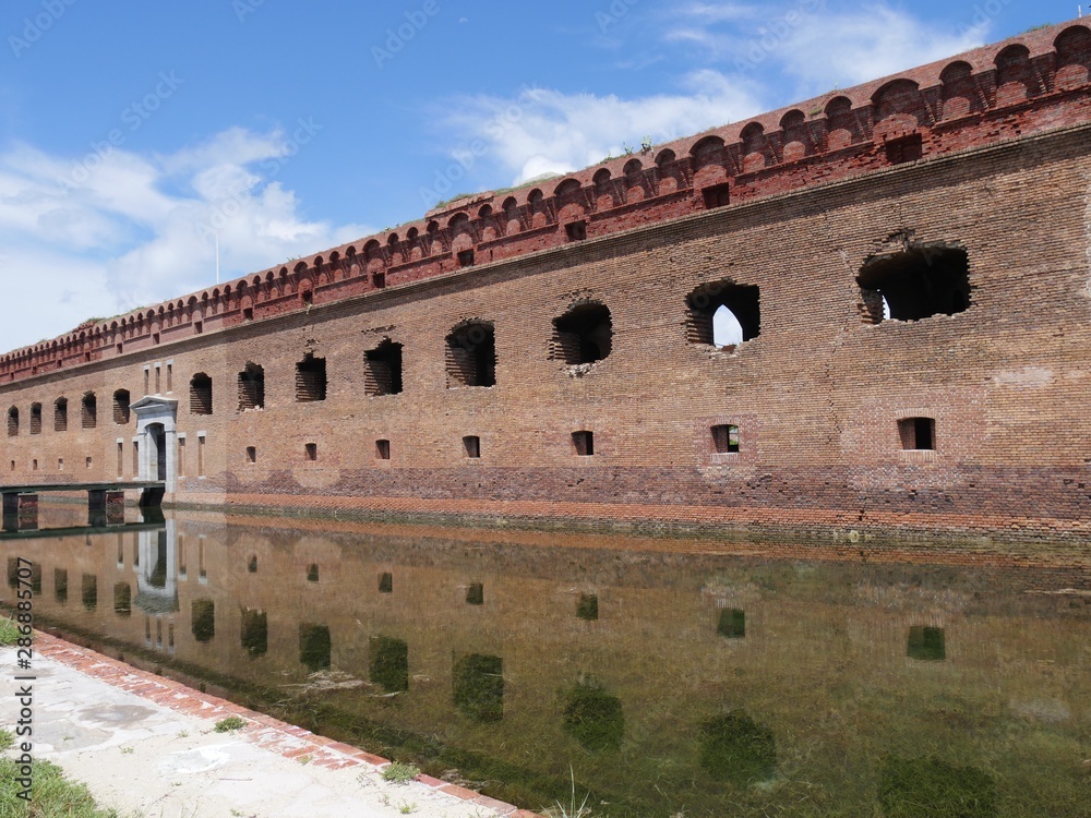 Medium wide side view shot of the entrance to Fort Jefferson, Dry Tortugas National Park in Florida, with the fort reflected in the moat waters.
