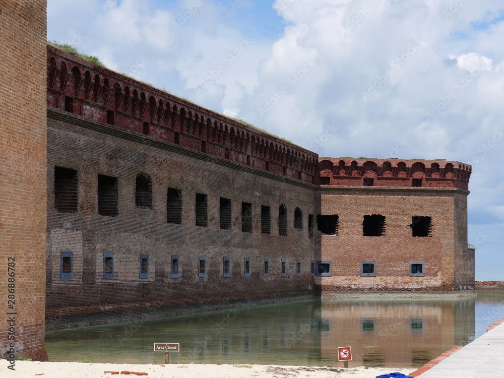 Moat reflecting one side of Fort Jefferson, with warning signs in the banks.