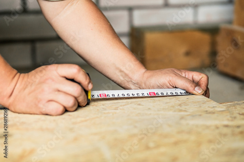 Builder measures OSB sheet during new home construction or renovation.