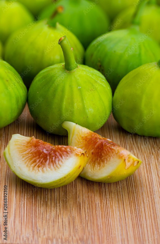 Whole and cut green figs, with fig leaves. Foreground. On wooden background. Whole and cut green figs, with fig leaves. Foreground. On wooden background.