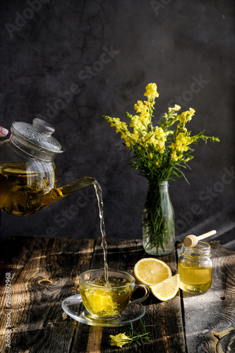 Herbal tea with lemon and honey in glass cup and teapot on sunny day light