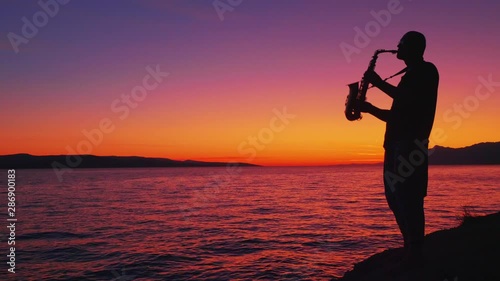 saxophonist plays against the backdrop of a beautiful sunset and the sea