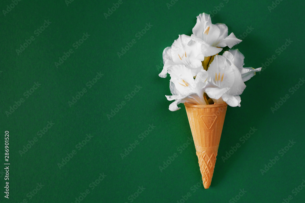 White gladioli in a waffle cone resembling creamy ice cream. Creative flower ice cream on a plain green background. Tasty floral card, botanical concept. Copy space, flat lay.