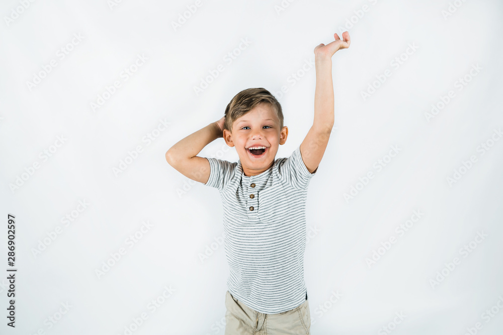 Little boy with autism standing on a white background feeling happy and smiling with his arms raised