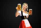 Happy sexy oktoberfest girl waitress, wearing a traditional Bavarian or german dirndl, serving two big beer mugs with drink isolated on black background.