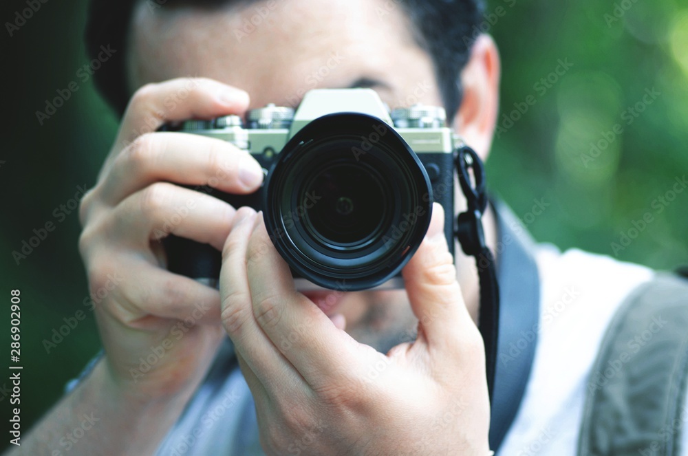 Close up portrait of young photographer taking photo, focusing at you.