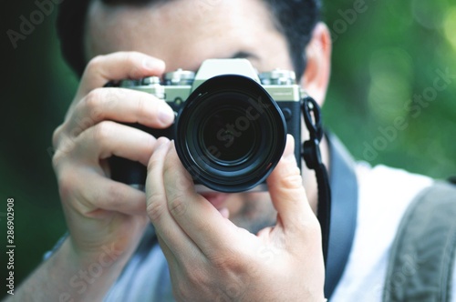 Close up portrait of young photographer taking photo, focusing at you.