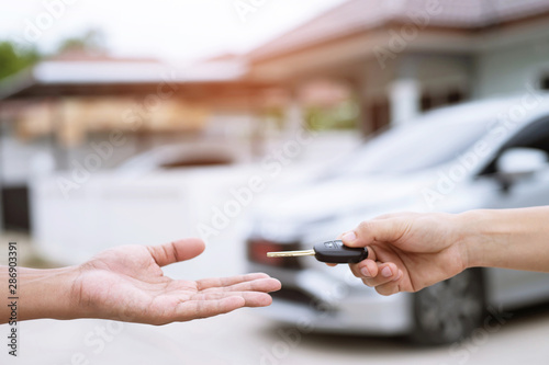 Car key  man handing over gives the car key to the other male on car an home background. Leave space to write a description of the message text.