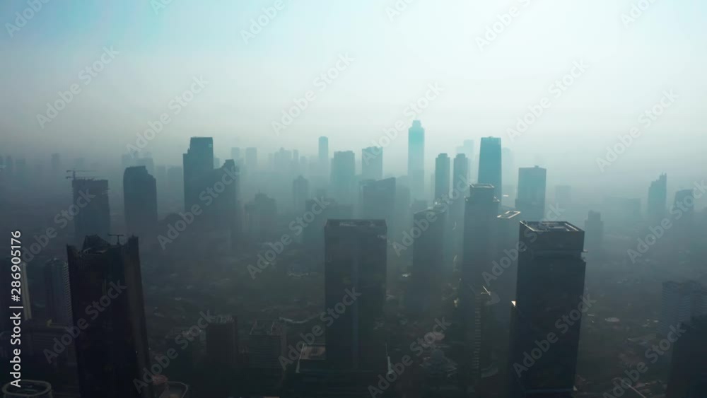 JAKARTA, Indonesia - August 27, 2019: Beautiful aerial landscape of silhouette of skyscrapers with dangerous air pollution fog at day. Shot in 4k resolution from a drone flying from left to right