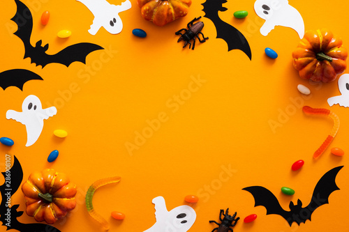 Happy halloween holiday concept. Halloween decorations, pumpkins, bats, candy, ghosts, bugs on orange background. Halloween party greeting card mockup with copy space. Flat lay, top view, overhead.
