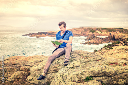 man sitting on the rocks reading an e-book by the sea