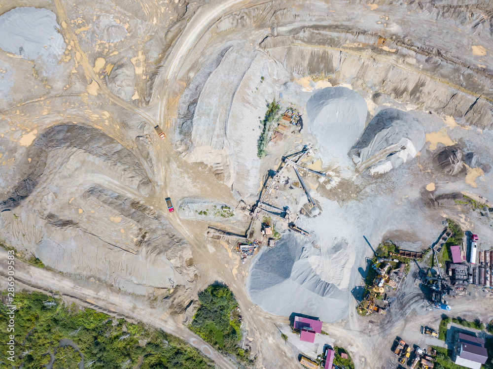 Aerial view of a small plant for the production and cleaning rubble and cement near the heaps of building materials from the pipe of which gray smoke goes, the tractor transports the finished product.