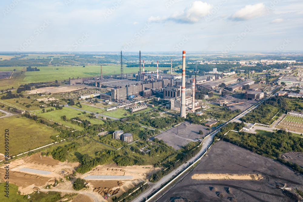 Aerial view of a large industrial plant with high pipes against a landscape with a blue sky and clouds. Environmental pollution and production.