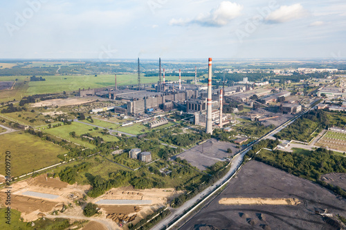 Aerial view of a large industrial plant with high pipes against a landscape with a blue sky and clouds. Environmental pollution and production.