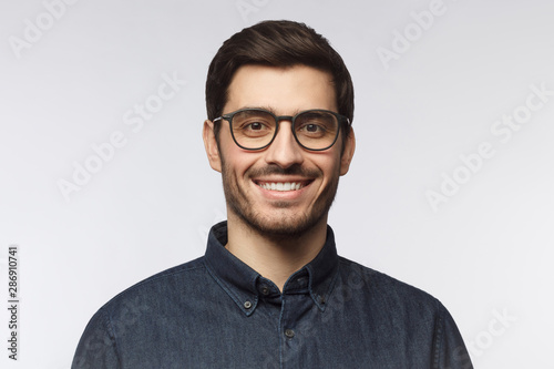 Headshot of cheerful handsome man with trendy haircut and eyeglasses isolated on gray background photo