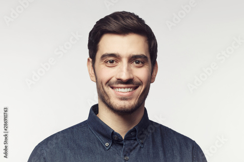 Close-up portrait of young smiling man in denim shirt isolated on gray background photo