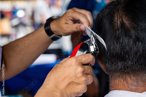 Hairdresser use comb and hair clipper doing haircut in community center.
