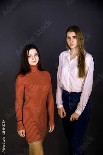 Two girls of different appearance.  Tall and short, blonde and brunette, in formal clothes and a red dress.  Shooting in the studio, plain background.