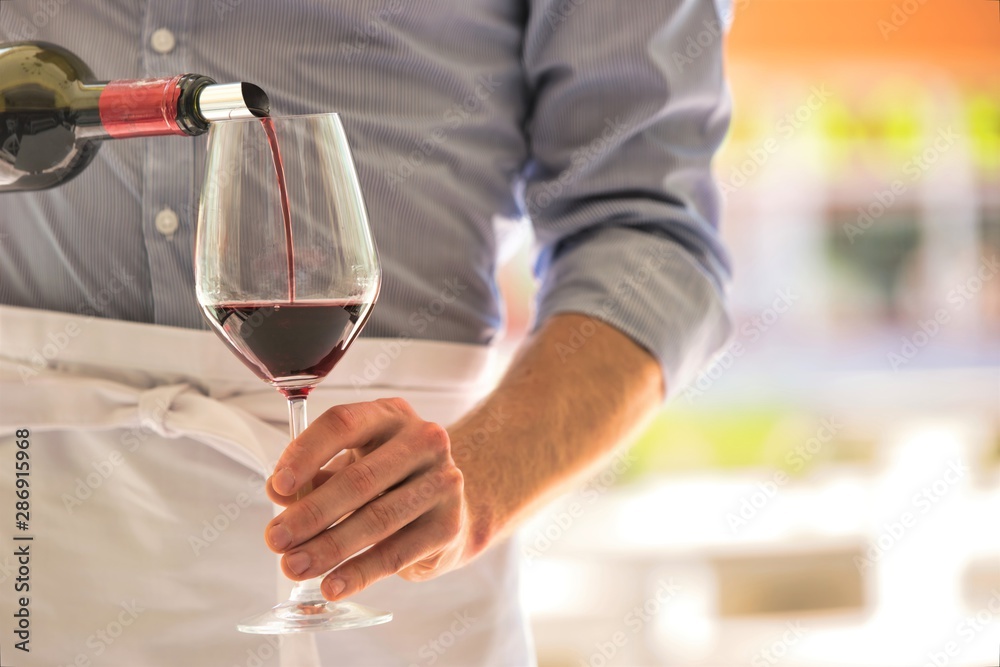 Midsection of waiter pouring red wine in wineglass at restaurant Midsection of waiter pouring red wine in wineglass at restaurant