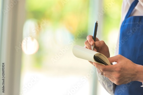Young confident waitress writing on notepad at restaurant