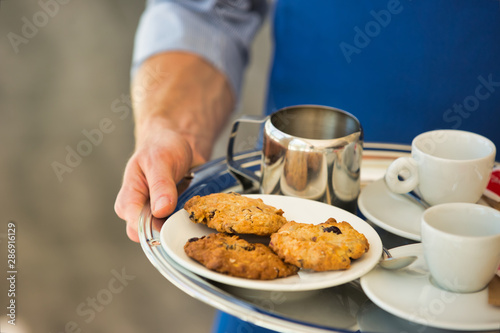 Young waiter serving coffee and cookies at restaurant © moodboard