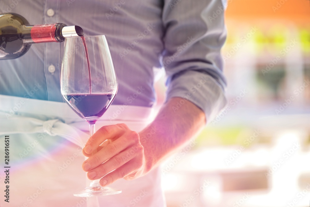 Midsection of waiter pouring red wine in wineglass at restaurant Midsection of waiter pouring red wine in wineglass at restaurant