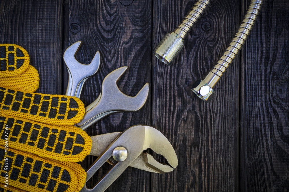 Fototapeta premium Plumbing tools and gloves for connecting water hoses on a black wooden background.