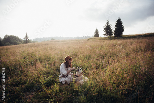 Girl and her friend dog are playing on the straw field background. Beautiful young woman relaxed and carefree enjoying a summer sunset with her lovely dog