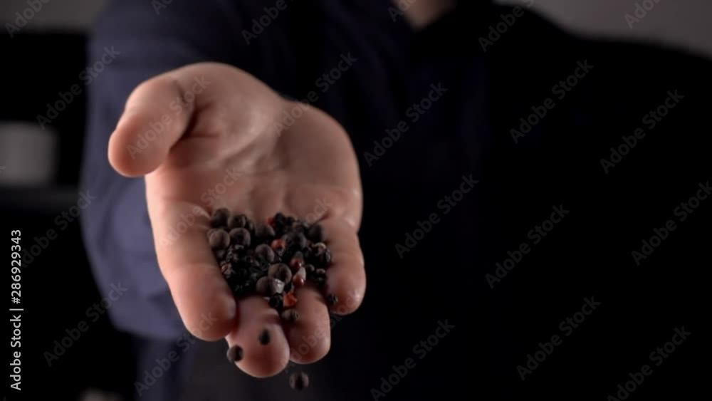 Black and red pepper falling from man's hand on dark background, cooking in slow motion side view Black and red pepper falling from man's hand on dark background, cooking in slow motion side view