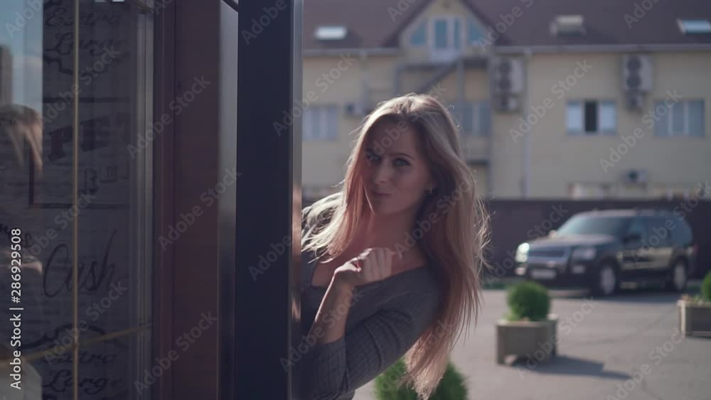 Cute young girl walks in an urban environment. A happy girl in a gray dress has fun, smiles, flirts and peers around the corner of the building. Cute young girl walks in an urban environment. A happy girl in a gray dress has fun, smiles, flirts and peers around the corner of the building.